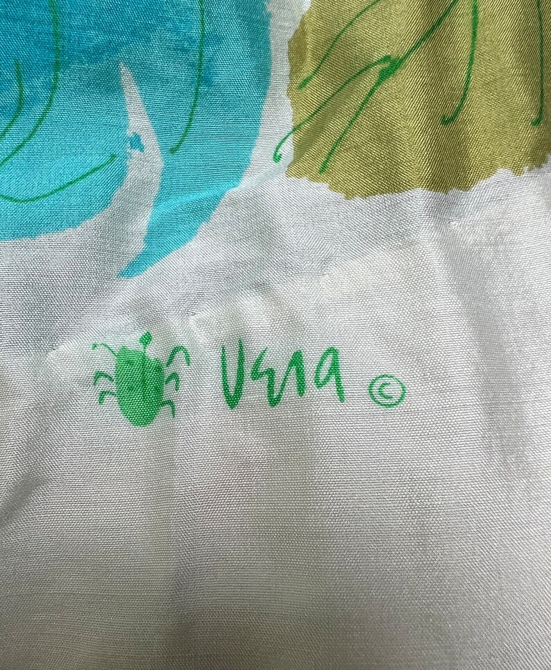 May include: A white fabric with a green bug and the word "Vera" written in green with a copyright symbol.