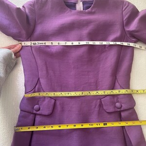 May include: A purple dress with long sleeves and a round neckline. The dress has two pockets on the front and a zipper in the back. The dress is measured with a tape measure, showing the length of the dress is 36 inches.
