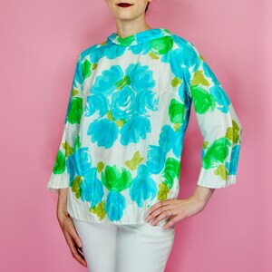 May include: A white blouse with a blue and green floral print. The blouse has a high neck and long sleeves.