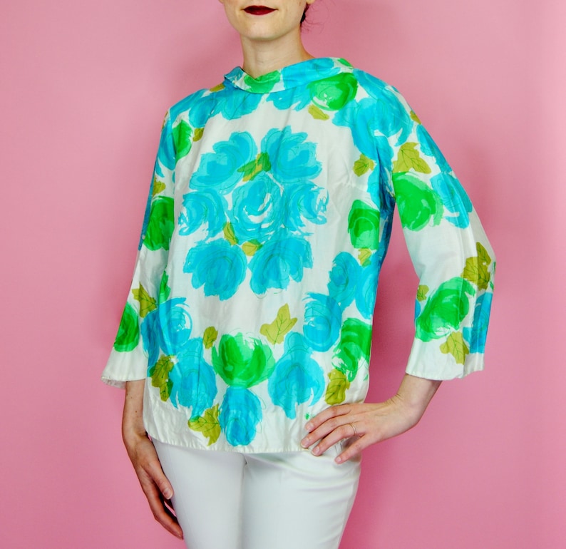 May include: A white blouse with a blue and green floral print. The blouse has a high neck and long sleeves.