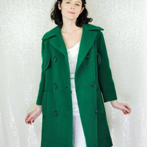 Pu&ograve; includere: Un lungo cappotto verde a doppio petto con colletto e tasche.