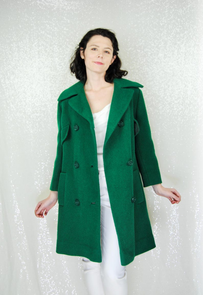 Pu&ograve; includere: Un lungo cappotto verde a doppio petto con colletto e tasche.