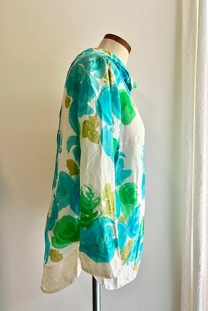 May include: A white blouse with a blue and green floral print. The blouse has a collar and long sleeves.