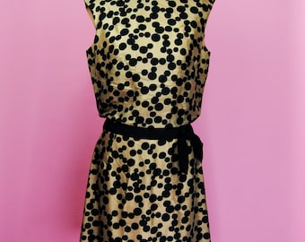 May include: A sleeveless dress with a black and gold polka dot pattern. The dress has a black sash tied at the waist.
