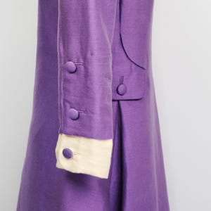May include: A purple dress with long sleeves and a white cuff. The dress has buttons on the sleeves and a seam down the back.