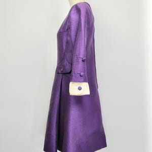 May include: A purple dress with a white trim on the sleeves and a button detail. The dress is on a mannequin.