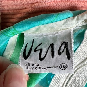 May include: A white tag with black text that reads "Usma" and "all silk dry clean" with a size 16 in a circle. The tag is attached to a turquoise and white patterned fabric.
