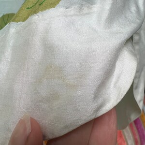 May include: White satin fabric with a light yellow stain. The fabric has a subtle texture and a slight sheen.