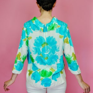 May include: A white blouse with a blue and green floral pattern. The blouse has a collared neckline and a zipper down the back.
