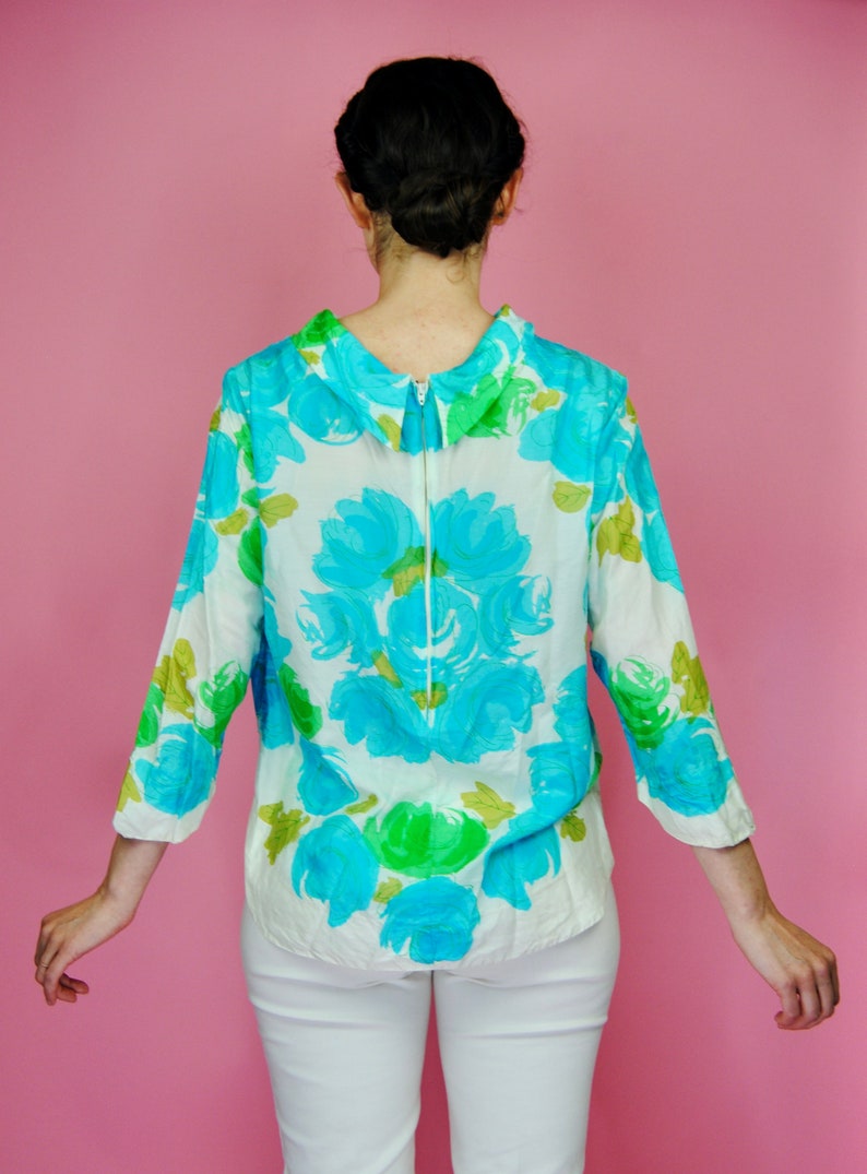 May include: A white blouse with a blue and green floral pattern. The blouse has a collared neckline and a zipper down the back.