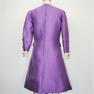 May include: A purple dress with long sleeves and a back zipper. The dress has white trim on the cuffs and buttons on the sleeves.