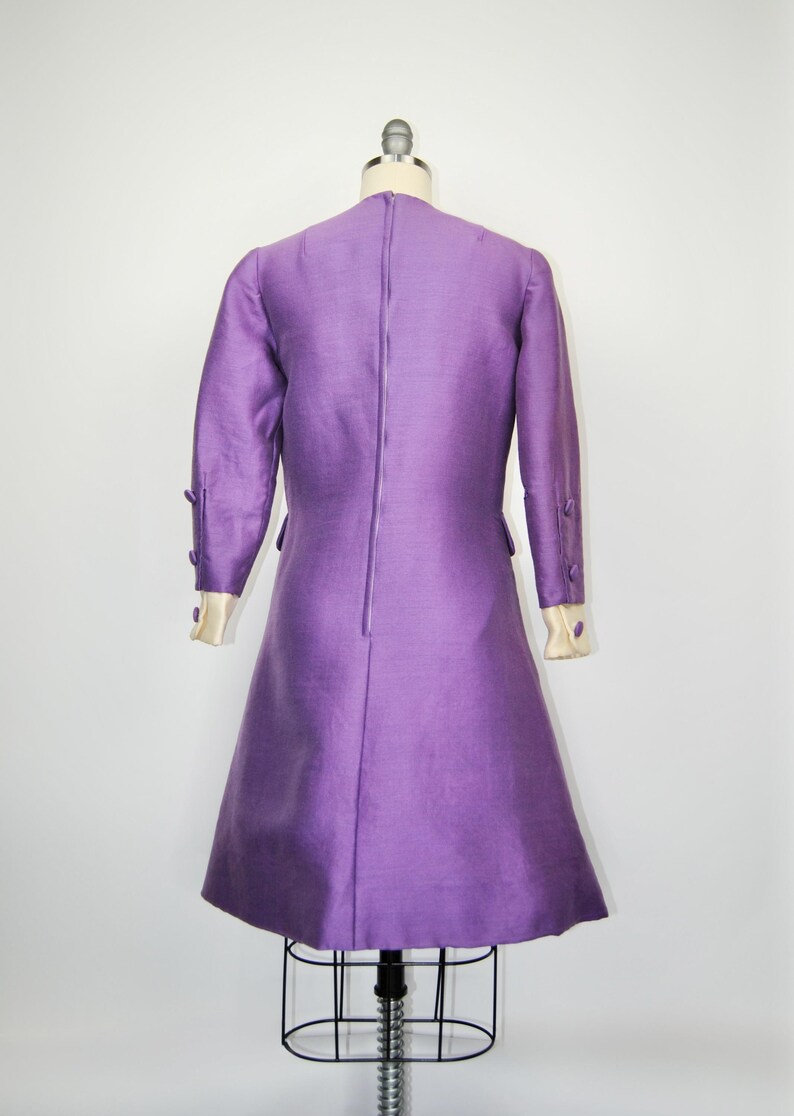 May include: A purple dress with long sleeves and a back zipper. The dress has white trim on the cuffs and buttons on the sleeves.