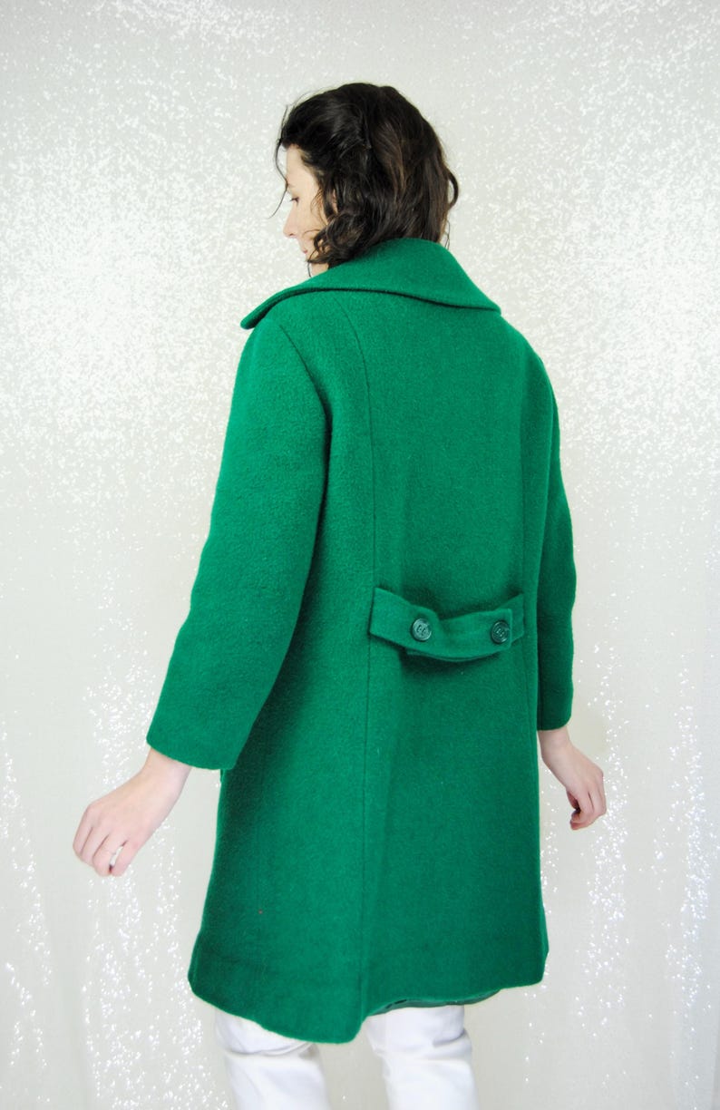 Pu&ograve; includere: Un lungo cappotto di lana verde con chiusura a doppio petto e due bottoni sul retro.
