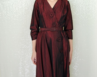 May include: A burgundy dress with a V-neckline, 3/4 sleeves, and a button closure. The dress has a belt at the waist and a slightly flared skirt.