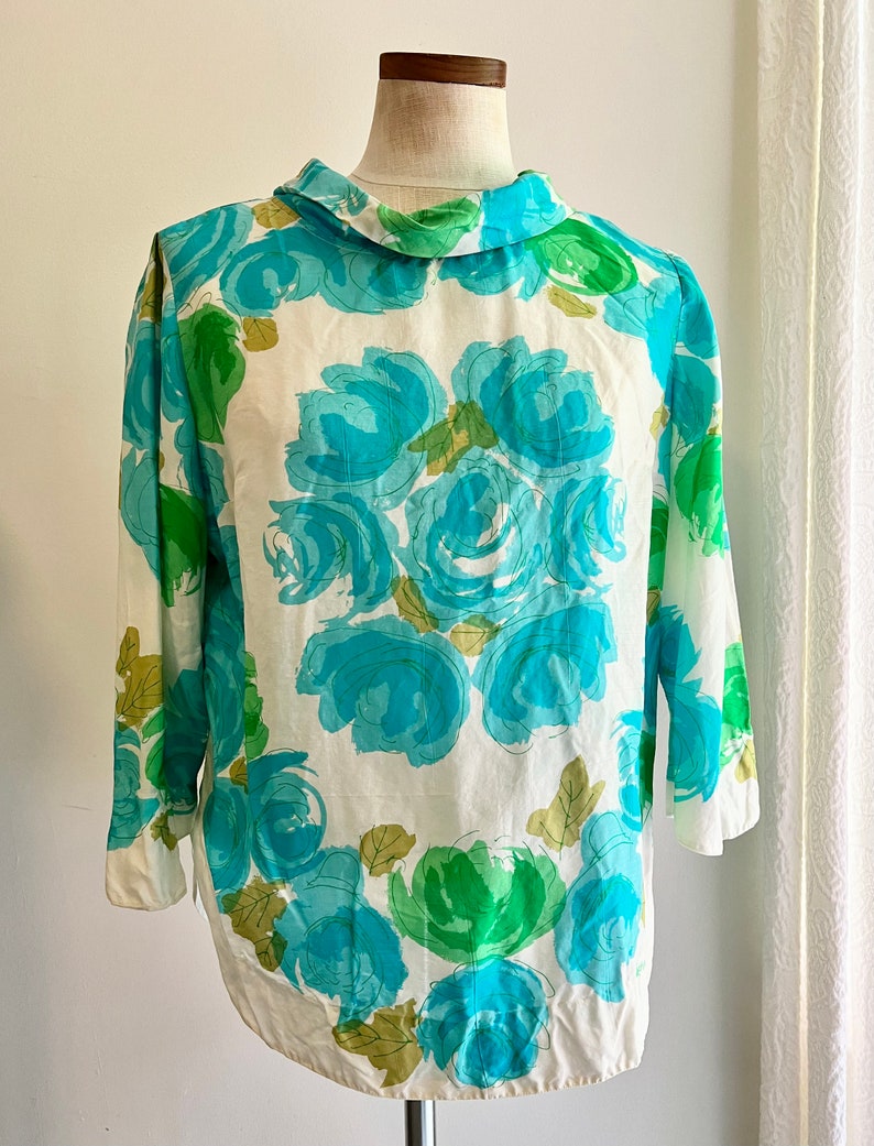 May include: A white blouse with a blue and green floral print. The print features large, abstract roses with a white background.