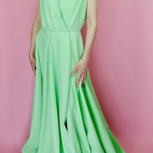 May include: A light green sleeveless maxi dress with a V-neckline and a wrap-style bodice. The dress has a flowing skirt with pleats and a slit in the front.