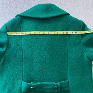 Pu&ograve; includere: Un cappotto di lana verde brillante con chiusura a doppio petto e due bottoni sul retro.