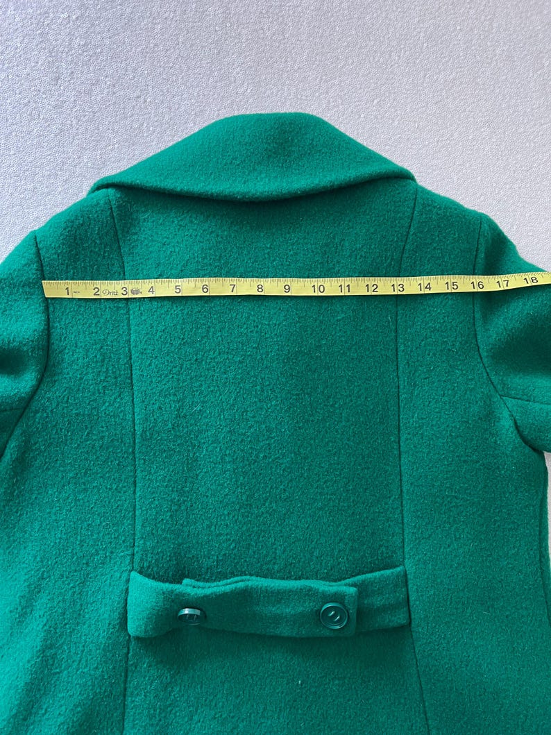 Pu&ograve; includere: Un cappotto di lana verde brillante con chiusura a doppio petto e due bottoni sul retro.