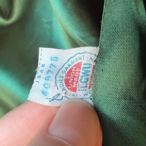 Pu&ograve; includere: Primo piano di un tessuto verde con un'etichetta bianca che dice "Ladies Garment Union Made in U.S.A." e "400775".
