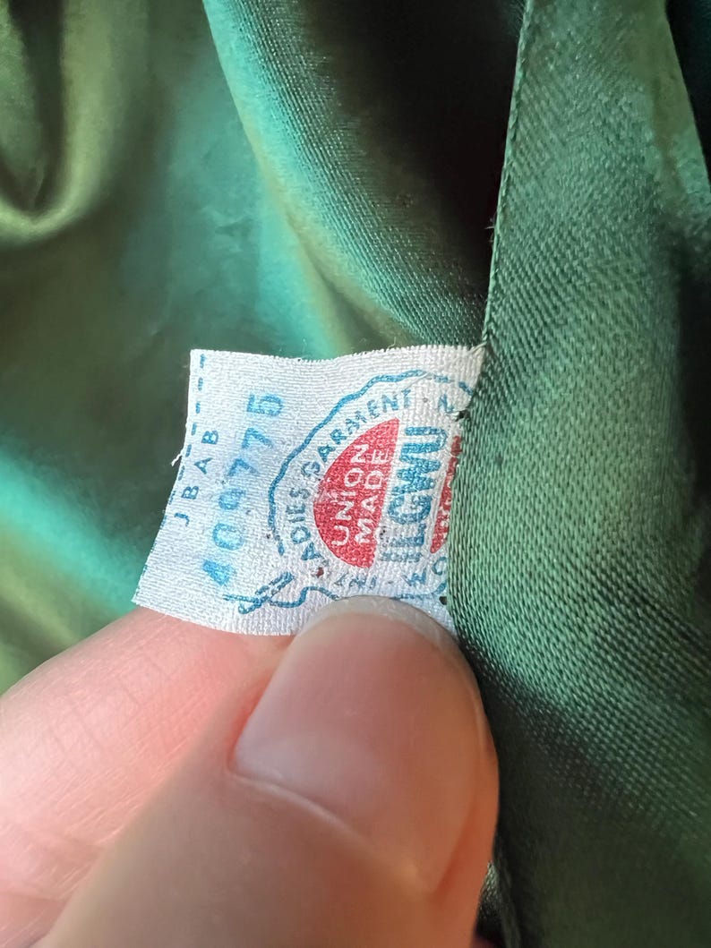 Pu&ograve; includere: Primo piano di un tessuto verde con un'etichetta bianca che dice "Ladies Garment Union Made in U.S.A." e "400775".