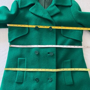 Pu&ograve; includere: Un cappotto di lana verde a doppio petto con due tasche su ogni lato e quattro bottoni sul davanti.