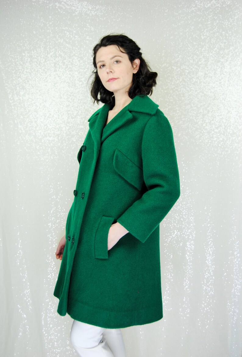 Pu&ograve; includere: Un lungo cappotto verde brillante a doppio petto. Il cappotto ha un colletto classico e due tasche.