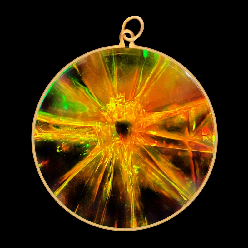 May include: A round, gold-toned pendant with a clear, iridescent, and textured glass center. The glass has a starburst pattern with a dark center.