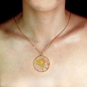 May include: A gold chain necklace with a round pendant featuring a yellow, green, and blue abstract design.
