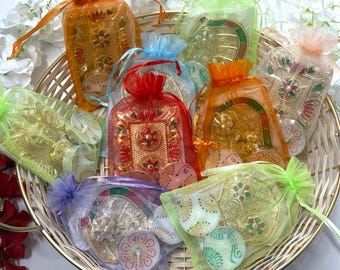 May include: A wicker basket containing various organza bags tied with ribbons. The bags are in shades of orange, green, and red, and hold ornate metal decorations. Some bags contain small, painted, round objects.