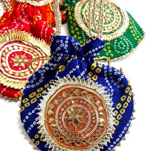 May include: Close-up of several colorful drawstring pouches. The pouches are in red, green, and blue, with intricate gold and silver embellishments. Each pouch has a beaded drawstring and a decorative circular design.