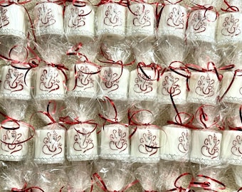 May include: Rows of white, cylindrical candles, each wrapped in clear cellophane and tied with a red ribbon. The candles feature a dark red, ornate design. The candles are arranged closely together, creating a pattern.