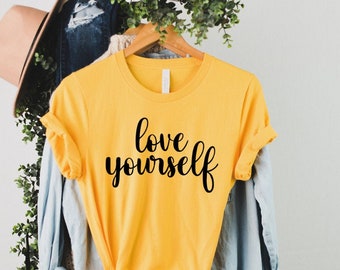 May include: Yellow t-shirt with the text "love yourself" in black script.