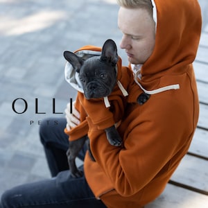 May include: A matching set of burnt orange hoodies with white drawstrings and white interior lining. One hoodie is sized for a person and the other is sized for a small dog. The text OLLI PETS is visible on the left side of the image.
