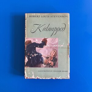 May include: A vintage paperback book titled "Kidnapped" by Robert Louis Stevenson. The cover features an illustration of two men in a dramatic scene, one holding a gun. The book is illustrated by William Sharp.