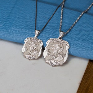 May include: Two silver necklaces with angel wing pendants. The pendants feature the words "Greenwood Police" and "Springfield Police" with corresponding badge numbers.