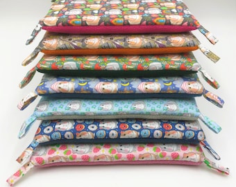 May include: A stack of ten colorful fabric cushions with different patterns featuring cartoon guinea pigs. The cushions are all rectangular and have a soft, plush texture.