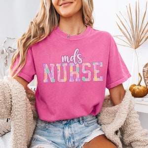 May include: Pink t-shirt with the text "mds NURSE" in a colorful, patterned font.