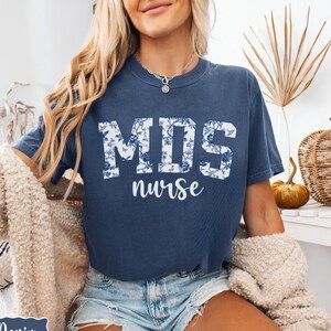 May include: A navy blue t-shirt with a white floral design that says "MDS nurse" in white letters.