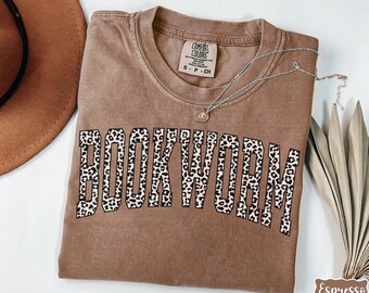 May include: A brown t-shirt with the word "BOOKWORM" printed in black letters with a leopard print pattern. The shirt is made of a soft, comfortable material.