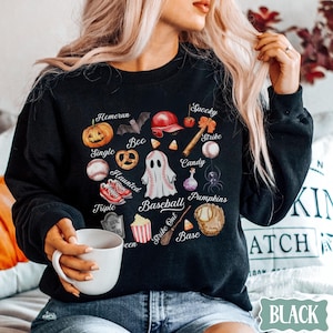 May include: Black sweatshirt with a Halloween baseball theme. The design includes a pumpkin, baseball, ghost, and other spooky elements. Text includes "Homerun", "Boo", "Haunted", "Spooky", "Strike", "Candy", "Baseball", "Pumpkins", "Strike Out", and "Base".