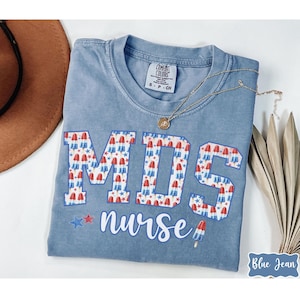 May include: A light blue t-shirt with a graphic of the letters "MDS" made up of red, white, and blue popsicles. The text "nurse" is below the letters.