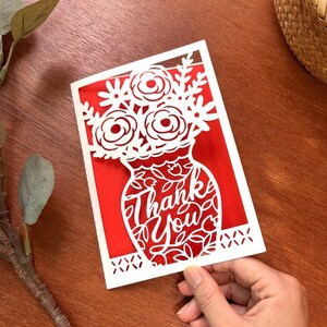 May include: White paper cut-out card with a red background. The card features a vase with flowers and the words "Thank You" in a decorative font.