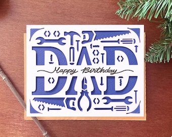 May include: A blue and white card with the word "DAD" cut out in the shape of tools. The card says "Happy Birthday" in cursive.