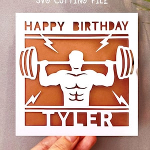 Op de afbeelding: Een witte papieren uitgesneden kaart met een bruine achtergrond. De kaart zegt "HAPPY BIRTHDAY TYLER" met een gewichtheffer grafiek. De woorden "Digital download SVG CUTTING FILE" staan bovenaan.