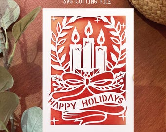 May include: A white paper Christmas card with a cut-out design featuring three lit candles, a bow, and the words "HAPPY HOLIDAYS." The background is a gradient of orange and red. The text "Digital download SVG cutting file" is at the top.