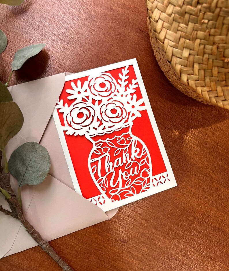 May include: A red card with a white cutout design of a vase with flowers and the words "Thank You".