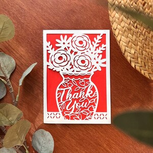 May include: White paper cut-out card with a red background. The card features a vase with flowers and the words "Thank You" inside the vase.