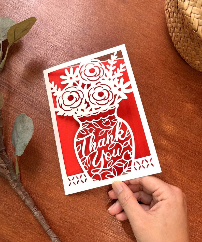 May include: White paper cut-out card with a red background. The card features a vase with flowers and the words "Thank You" in a decorative font.