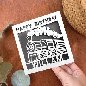 May include: White card with black cut-out design of a train with smoke and the words "Happy Birthday William".
