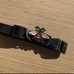 Op de afbeelding: Zwarte hondenriem met een geborduurde bij-patch in zwart en rood.